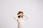 An image of a light-skinned woman raises her arms and covers her eyes with both her hands. The woman has curly light brown hair, gold hoops and a cream-colored long sleeve shirt. The title, How to Cope with Seasonal Depression is over the image