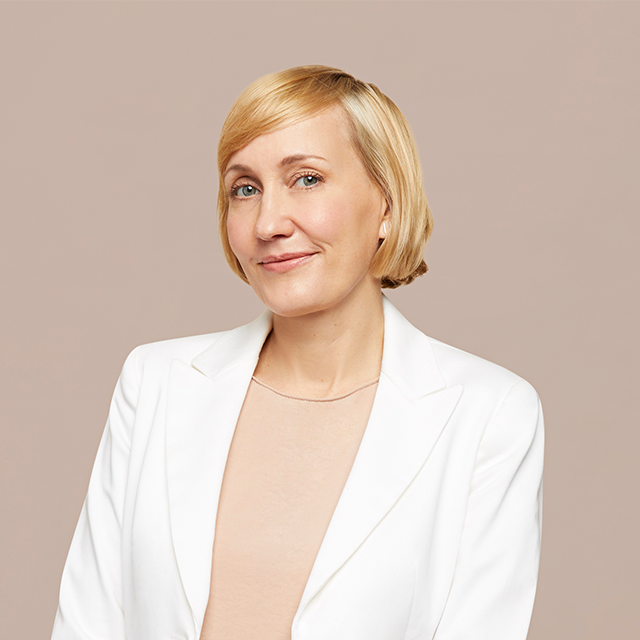 An image of Jessica Sowards, MS, LAc. She has a short blonde bob, green eyes and pale skin. She is wearing a white coat and tan shirt. She has a slight grin, looking forward.