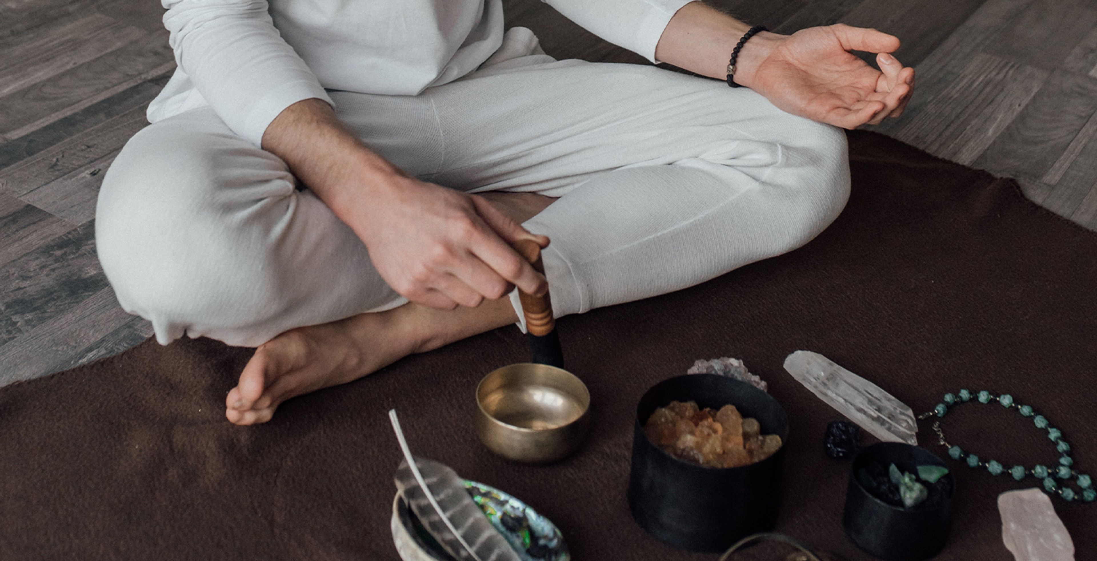Cross-legged person sits with bowls on the floor in front of them.