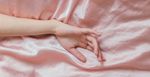 A white hand rests outstretched on a pink satin sheet