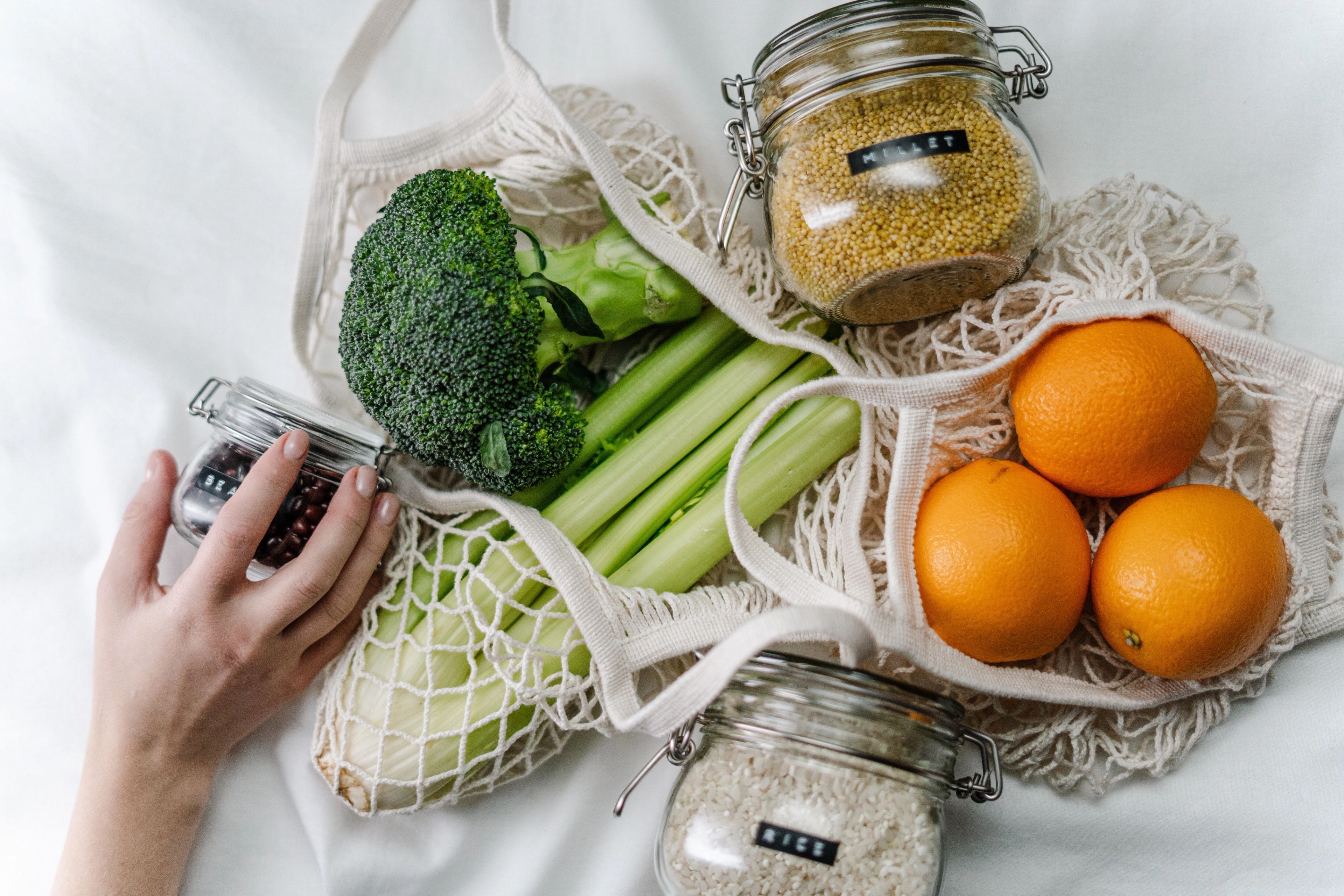 Broccoli, celery and oranges in reusable shopping bags, with grains in reusable glass jars