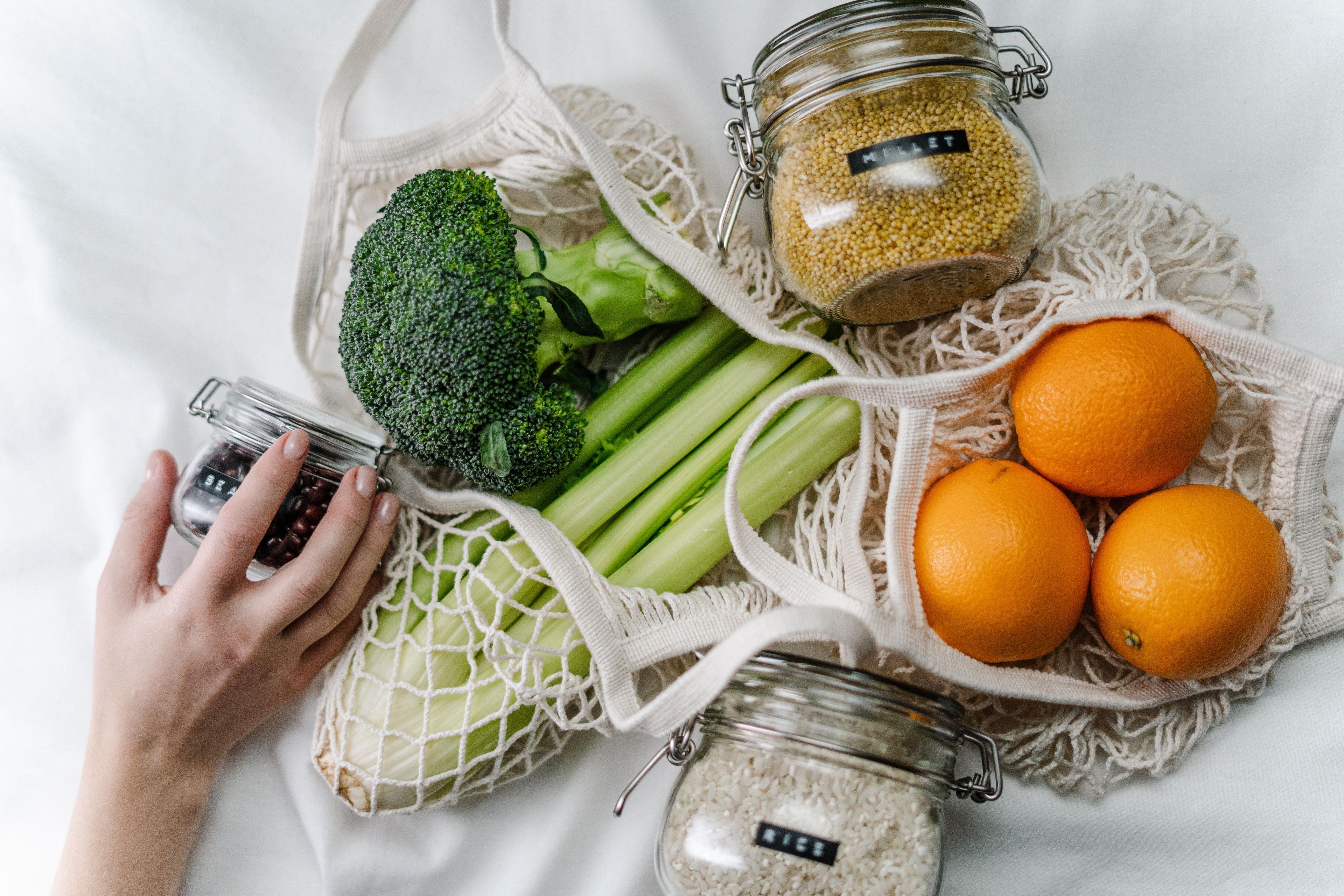 Broccoli, celery and oranges in reusable shopping bags, with grains in reusable glass jars