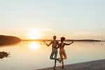 Two women hold a yoga pose while looking out at a sunset over a lake.