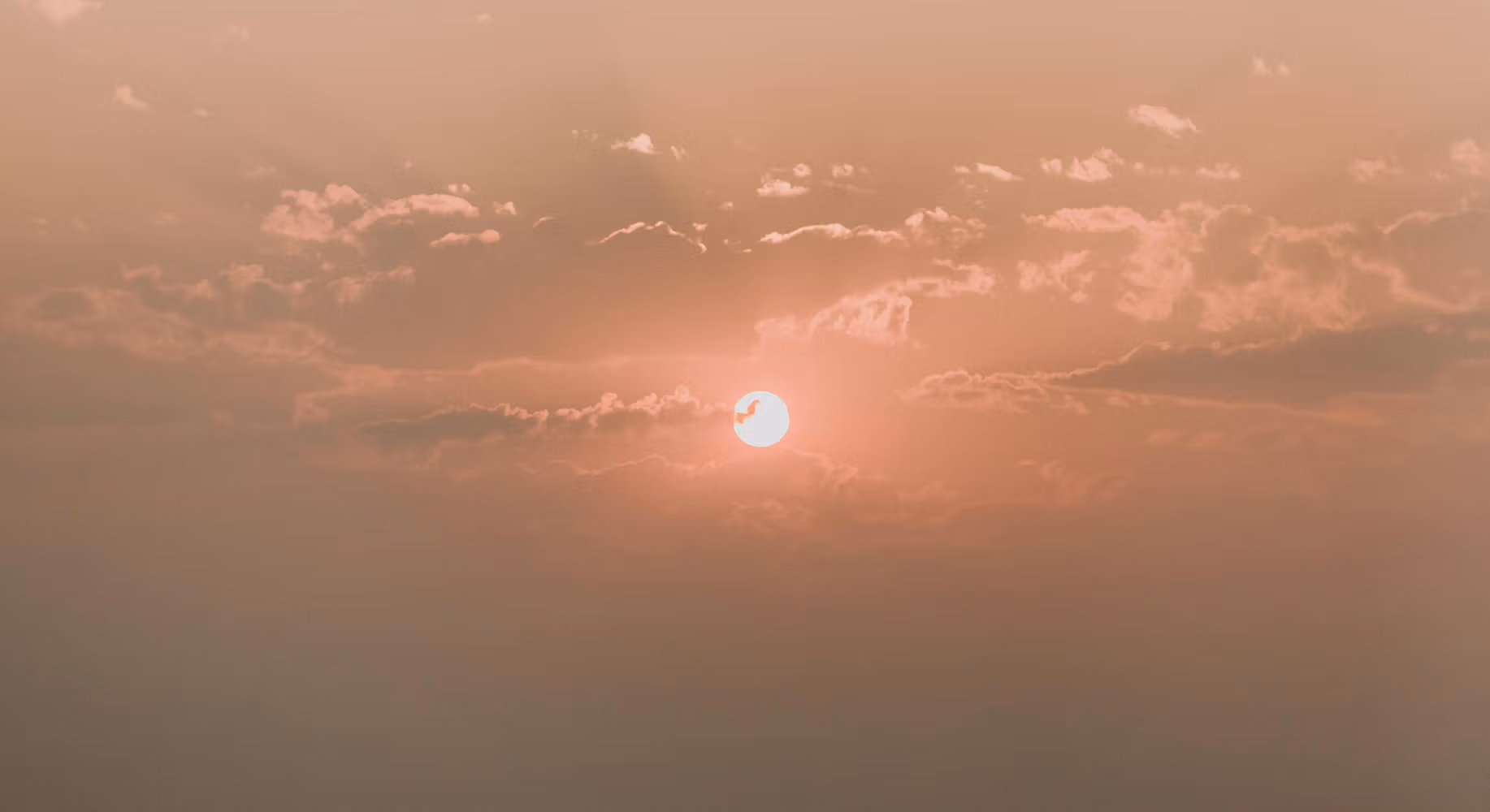 Image of red sun setting with cloud coverage over a sky with hues of pink and orange