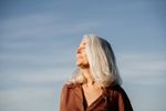 Grey haired woman with eyes closed, standing in front of a blue sky