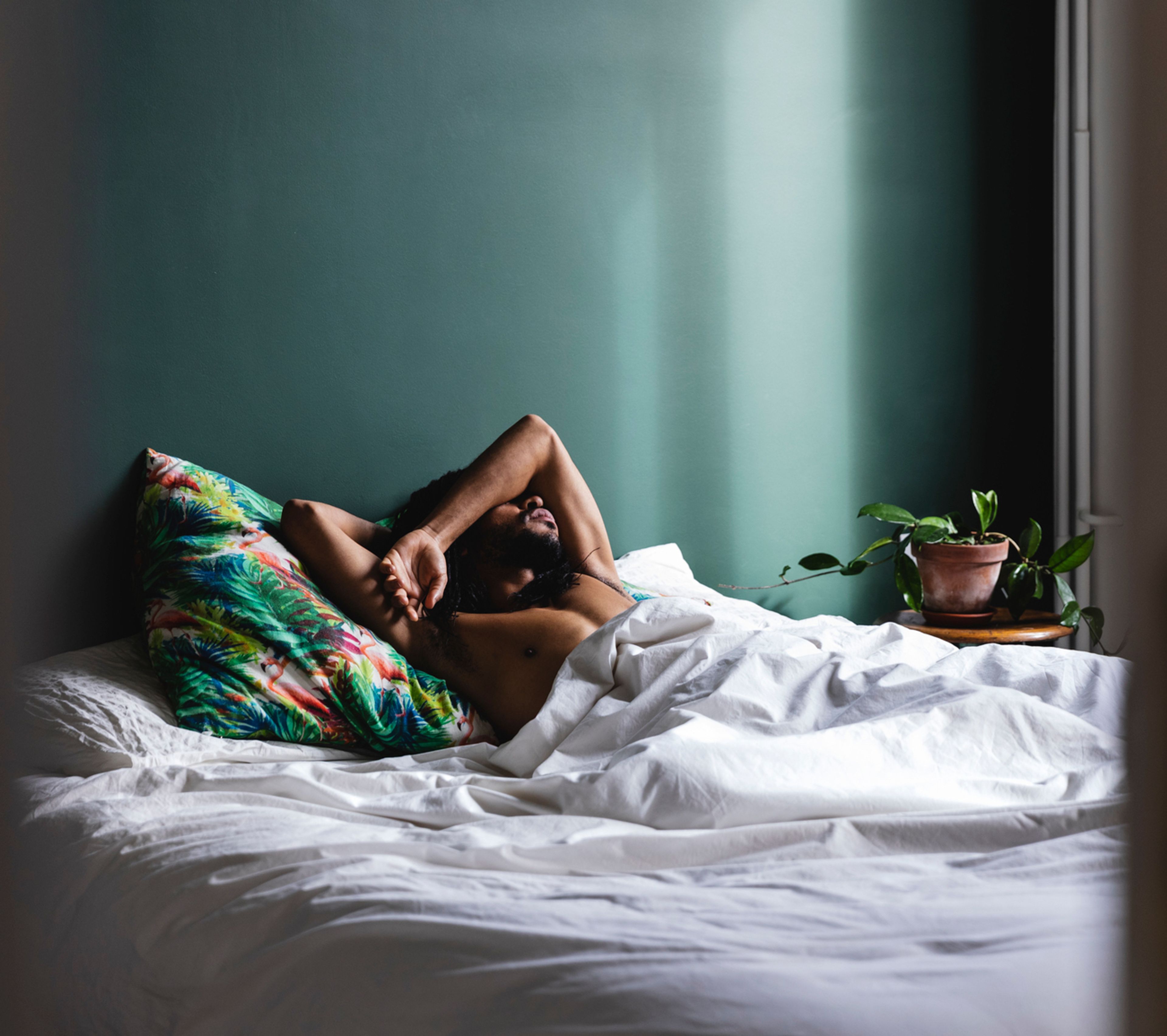 man in bed covering face with arms 