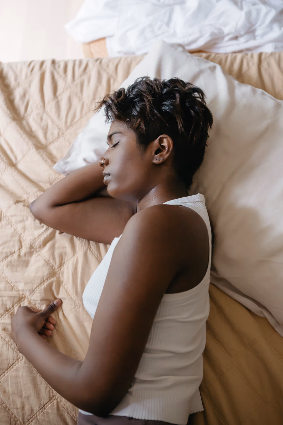Woman in a white tank top asleep on a bed