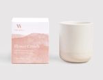 On the left, there is a white rectangular box with a rose pink paint sponge design. A rose-pink THE WELL logo on the top left corner of the box and white text on the pink paint design that reads Flower Crown, Cedarwood, Ylang Ylang, Geranium, 100% Natural Botanical Candle, 11 oz/312 g. On the right of the box is a cream-colored candle vessel.