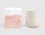 On the left, there is a white rectangular box with a rose pink paint sponge design. A rose-pink THE WELL logo on the top left corner of the box and white text on the pink paint design that reads Flower Crown, Cedarwood, Ylang Ylang, Geranium, 100% Natural Botanical Candle, 11 oz/312 g. On the right of the box is a cream-colored candle vessel.