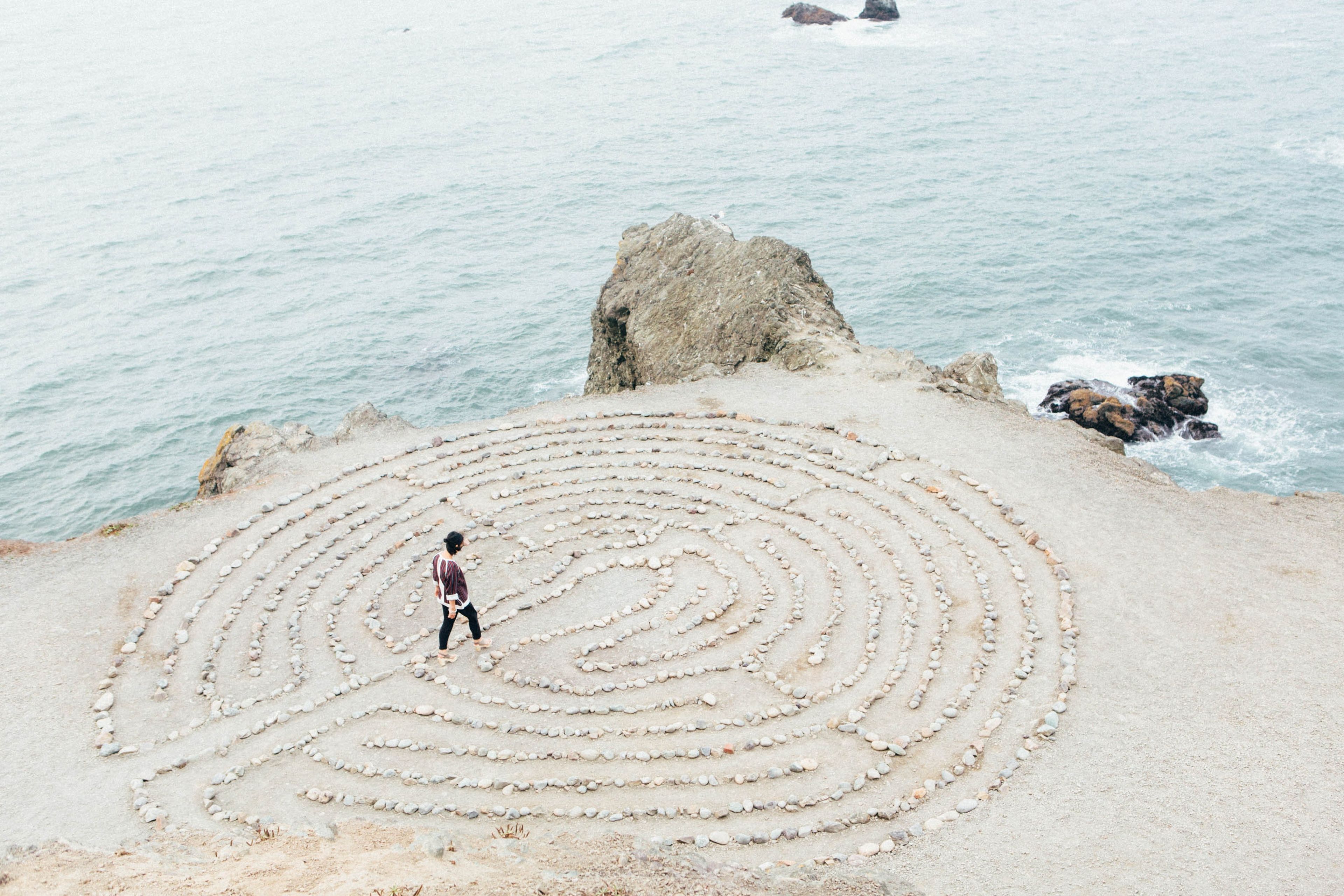 woman walking through maze of stones on a cliff above the beach