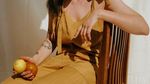 Woman sitting in a wooden chair holding a lemon and an orange.