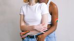 Two women with rainbows painted on their arms embrace.