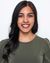 An Indian woman with red lipstick, brown eyes, dark brown hair and wearing a green shirt. She is smiling with her front teeth showing, looking forward. 