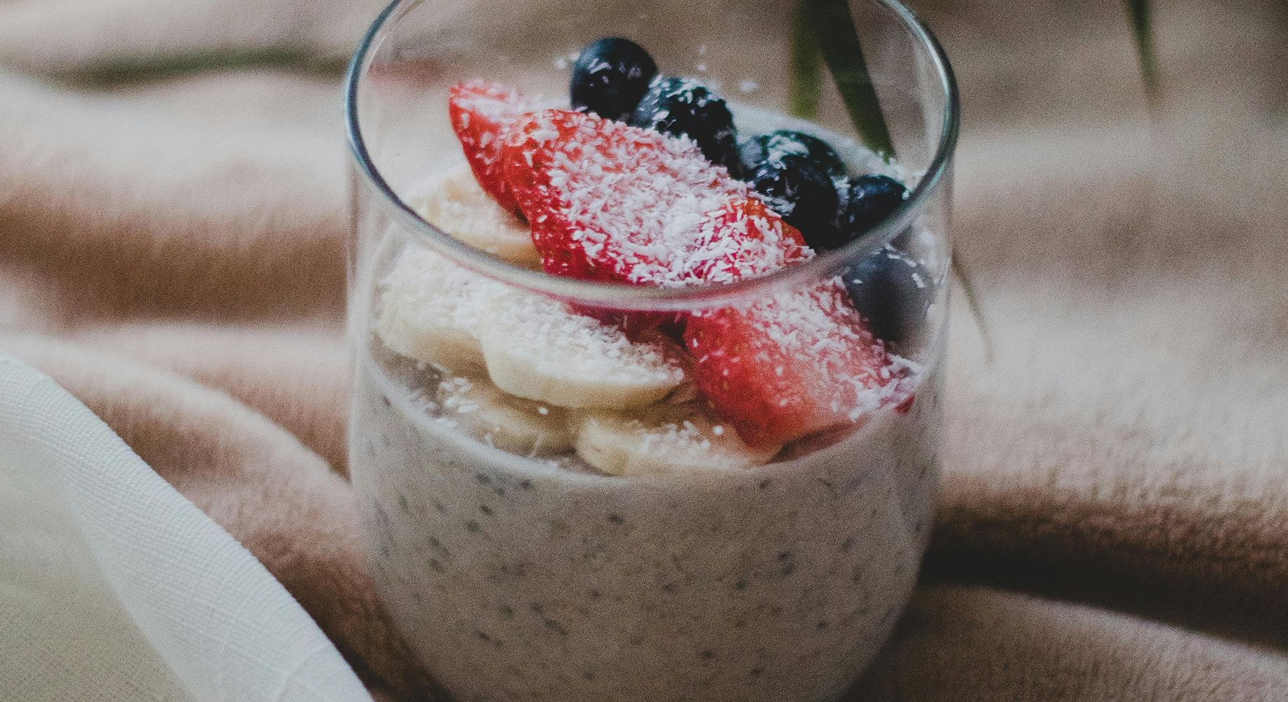 Glass cup with bananas, strawberries, blueberries and coconut flakes — fresh, whole-food nutrition