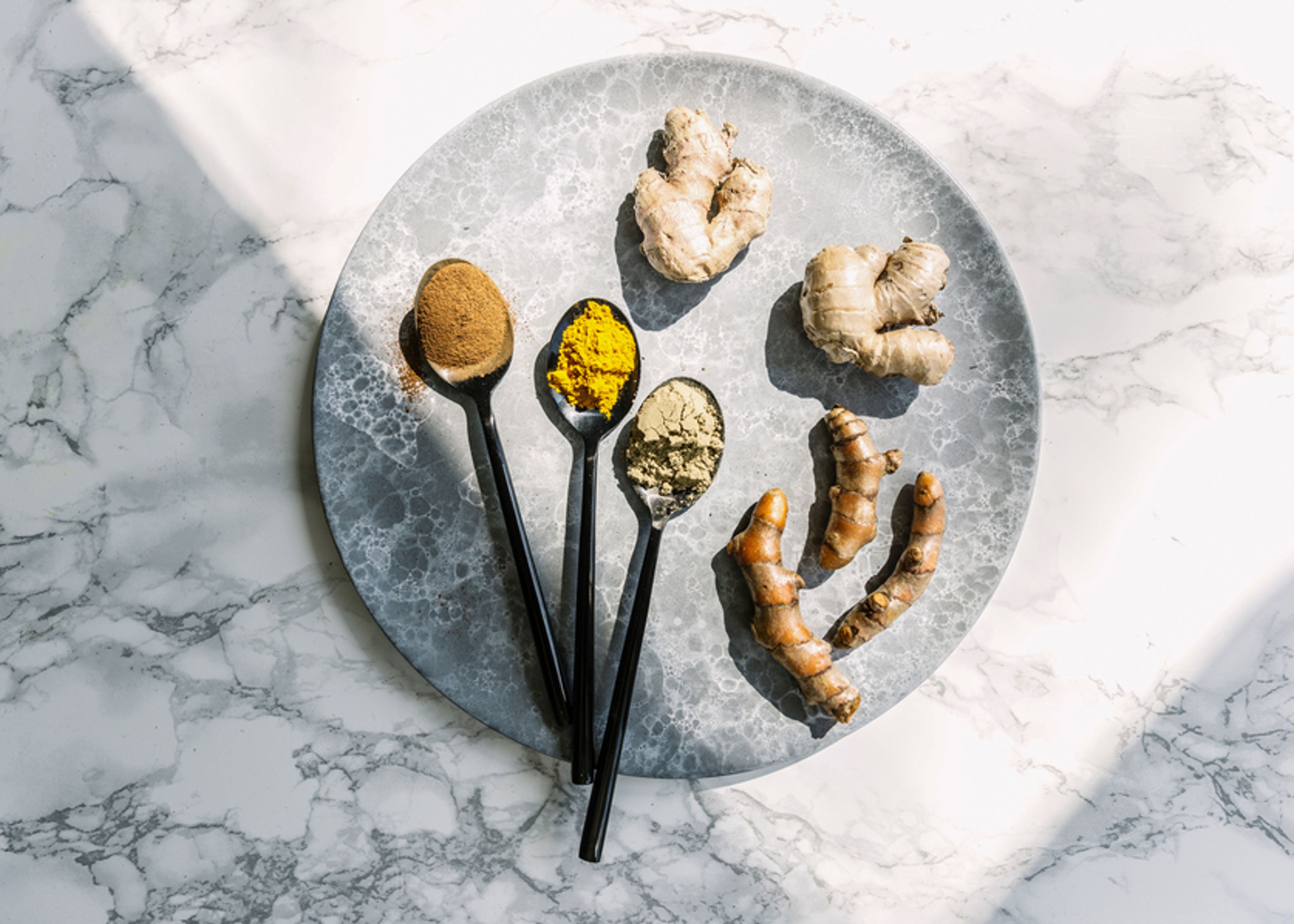 Spoons with spices and pieces of ginger and turmeric on platter