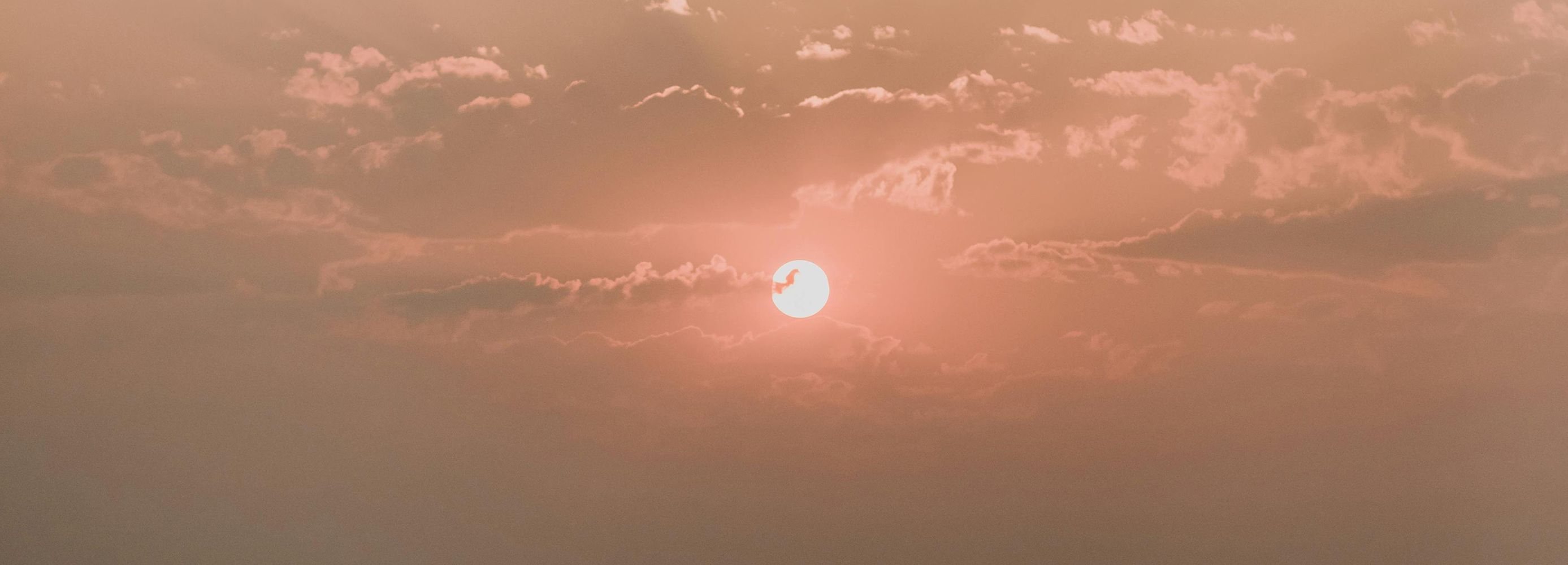 Image of red sun setting with cloud coverage over a sky with hues of pink and orange