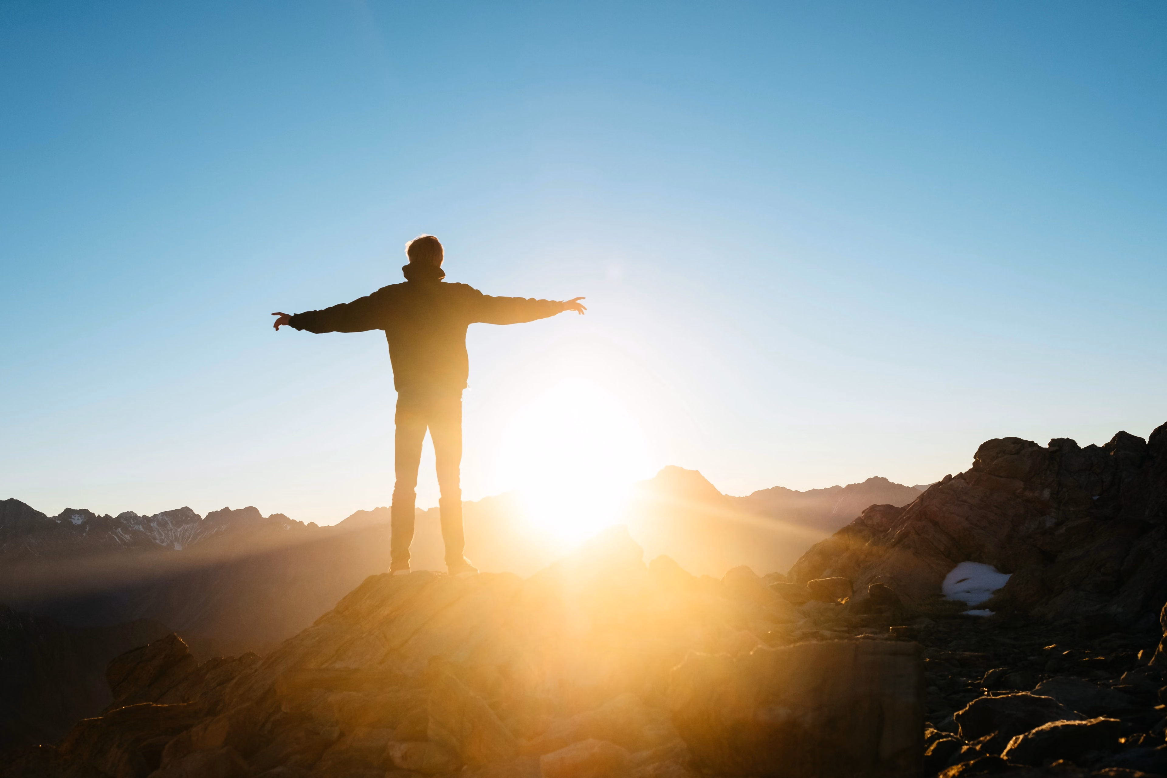 Man stands on a mountain with arms extended towards the sun.