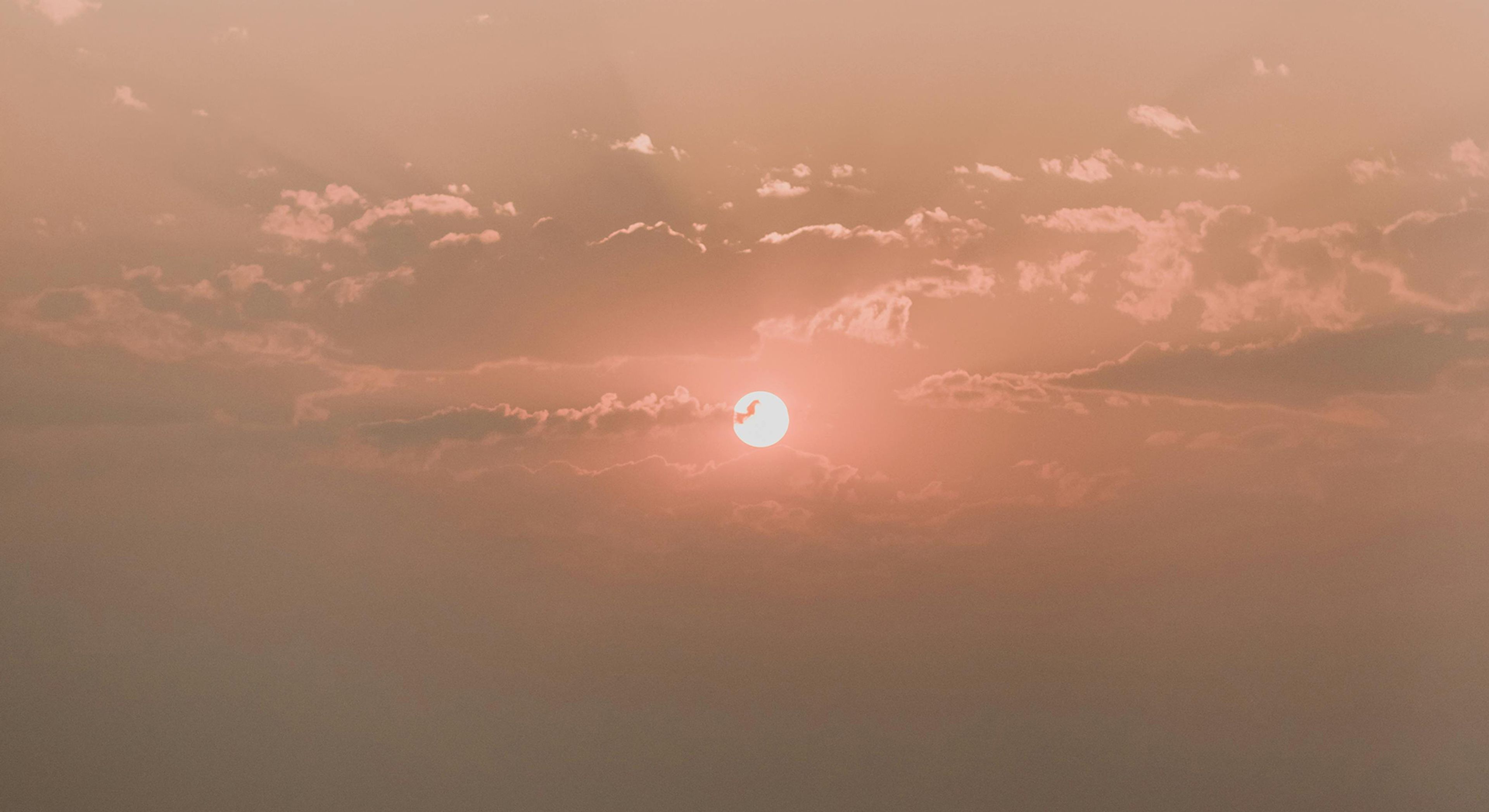 Image of red sun setting with cloud coverage over a sky with hues of pink and orange