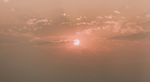 Image of red sun setting with cloud coverage over a sky with hues of pink and orange