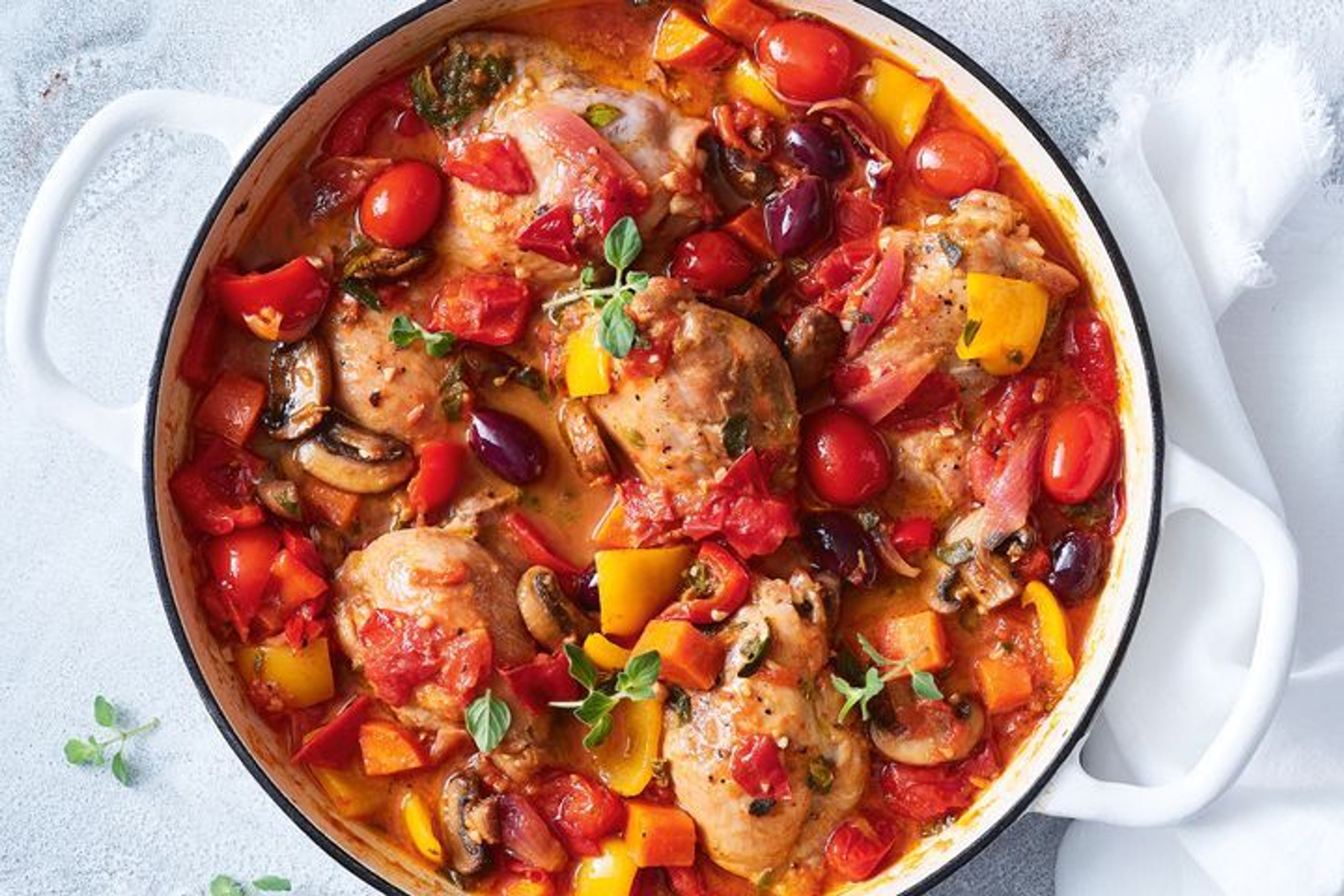 Chicken cacciatore in a white pot on top of a table covered in a white table cloth.