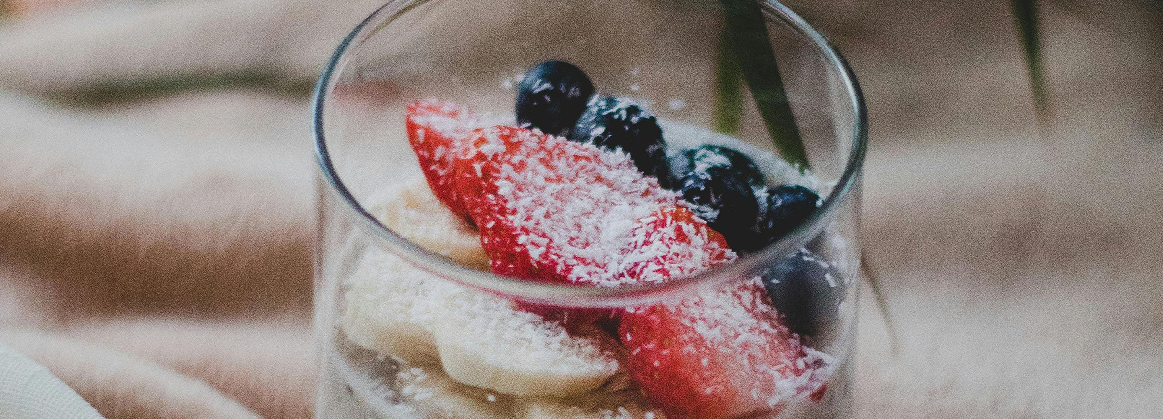 Glass cup with bananas, strawberries, blueberries and coconut flakes — fresh, whole-food nutrition