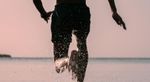 Man running with large body of water in the background, his left foot is splashing water