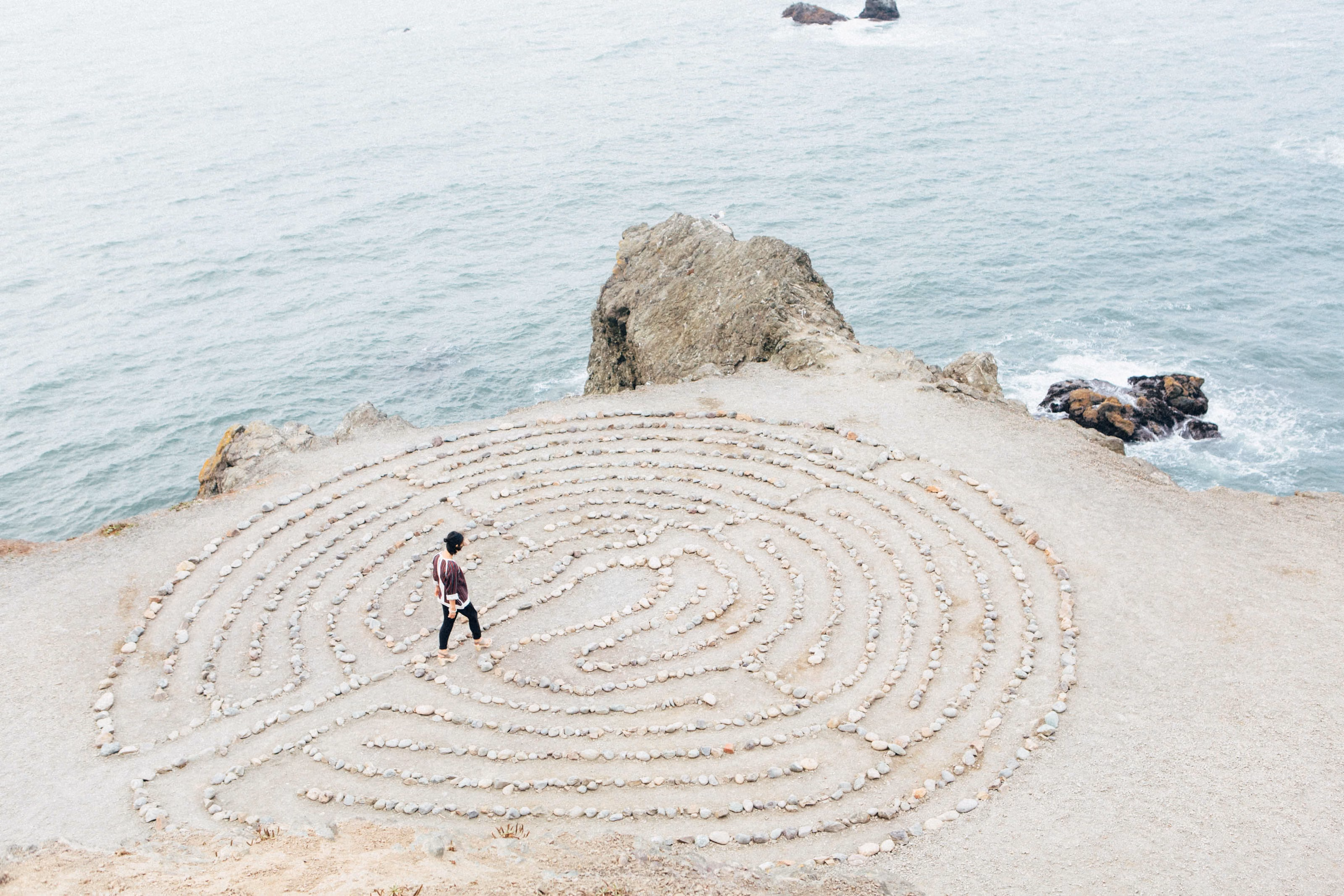 woman walking through maze of stones on a cliff above the beach