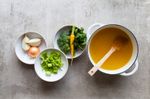 pot of bone broth with bowls of celery, broccoli, carrots, onions