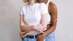 Two women with rainbows painted on their arms embrace.