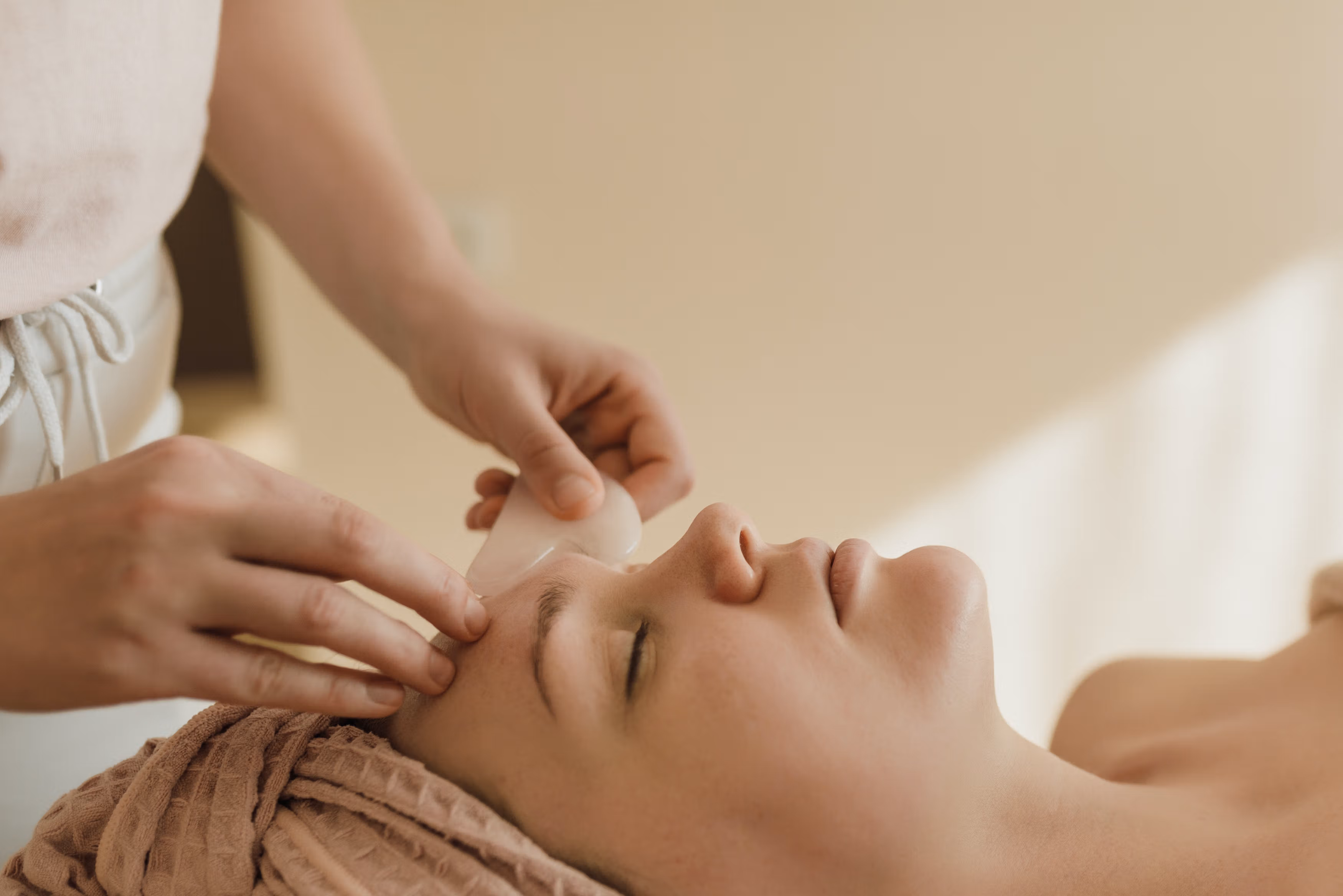 Woman lying on massage table getting a facial gua sha treatment