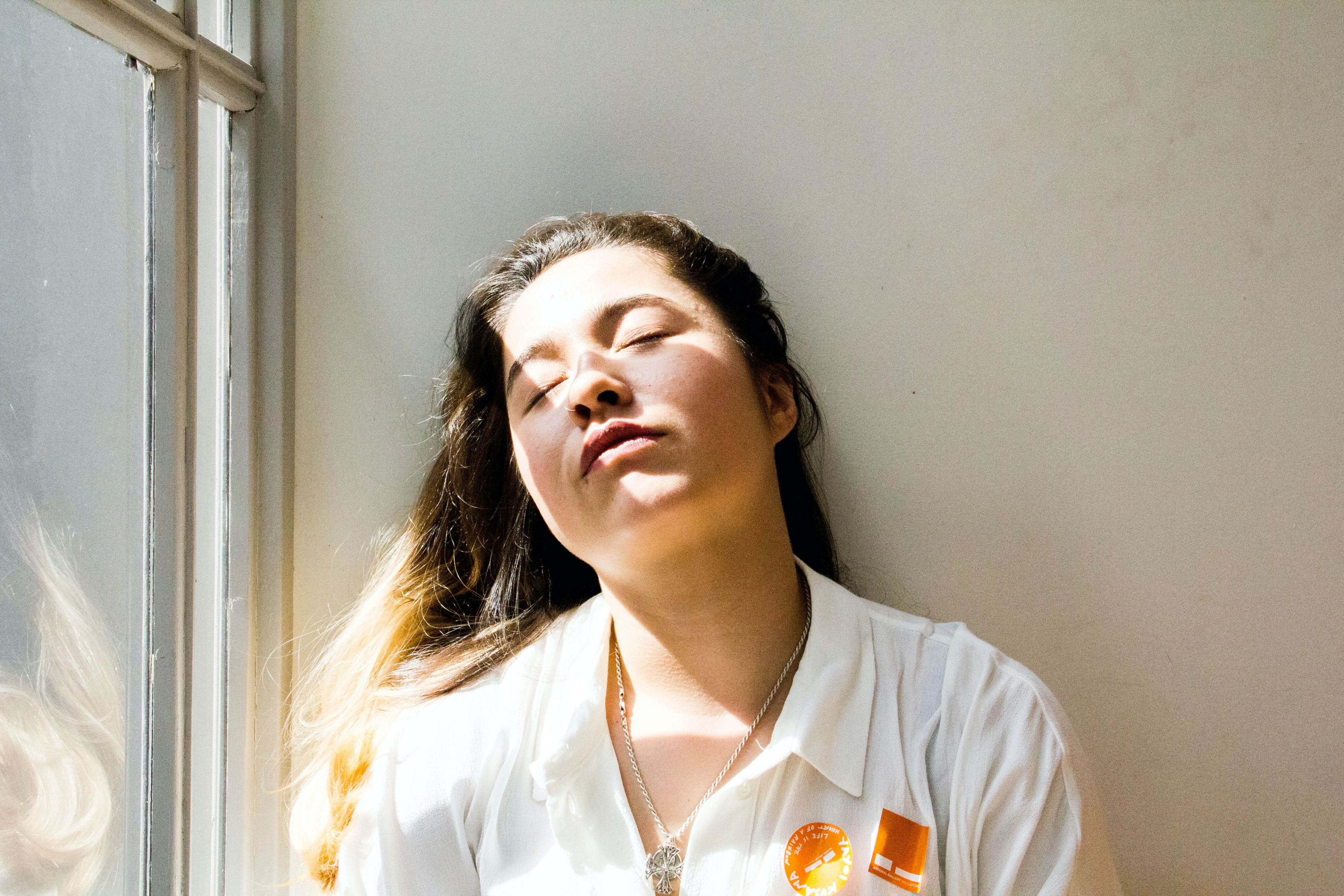 Woman leaning against wall with light from a window falling on her face.
