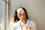 Woman leaning against wall with light from a window falling on her face.